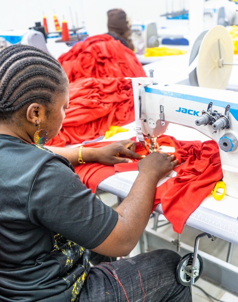 A Kintela seamstress sewing red garments at an industrial machine